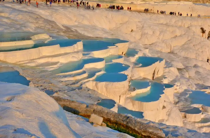 Pamukkale travertenleri ve turkuaz renkli doğal su havuzları üzerinde yürüyen ziyaretçiler